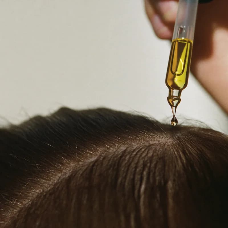 Goutte d'huile déposée sur la raie, à la racine des cheveux